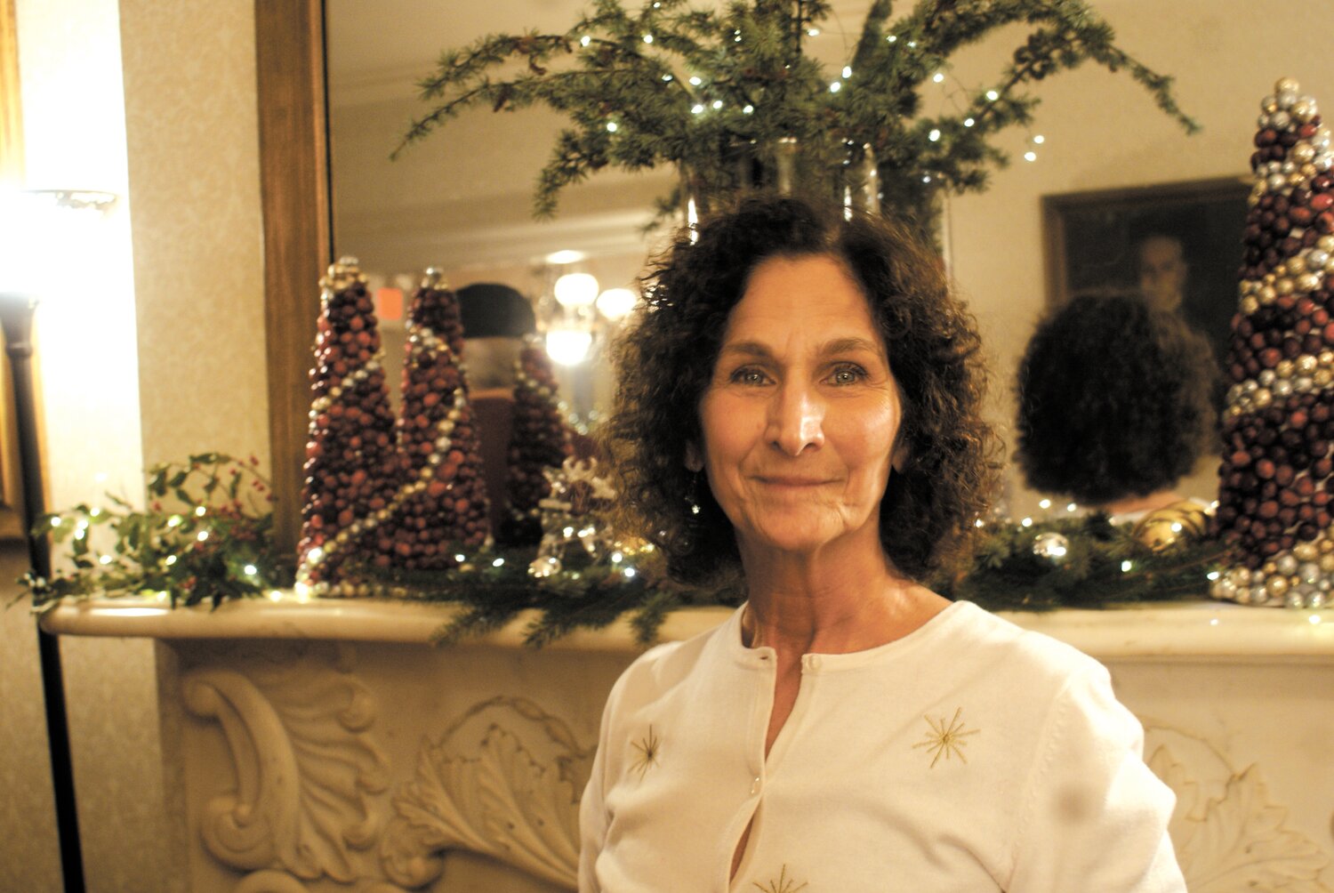 CROWNED WITH BOUGHS: Western Cranston Garden Club President Cheryle Celest standing in front of just a few of the decorations her organization provided for Sprague Mansion this season.